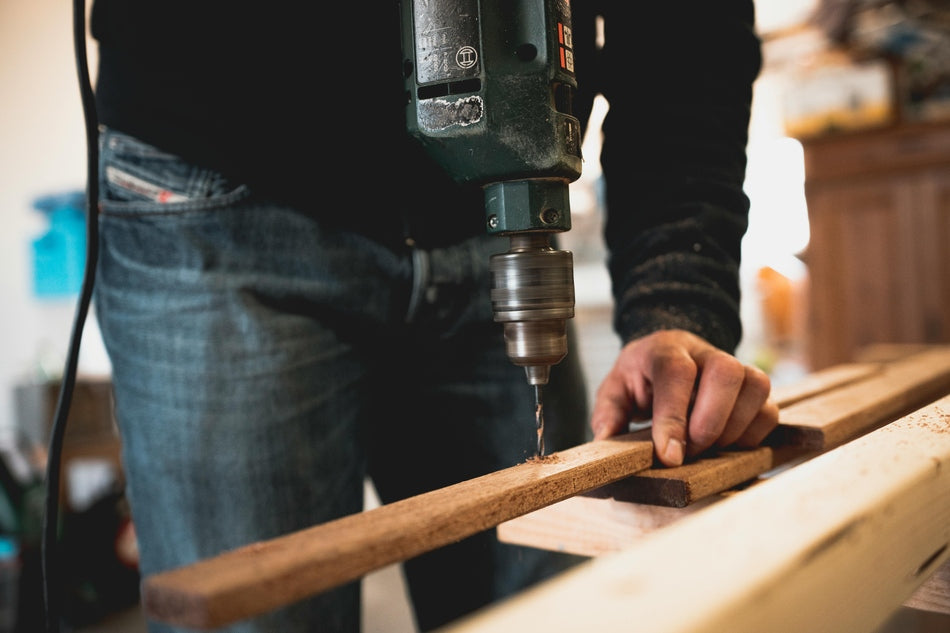 A man drilling on a workbench with a butcher block top.